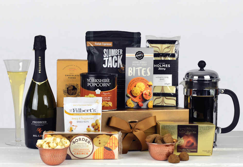 A bottle of prosecco with tasty food such as toffee popcorn, biscuits, french truffles, cheesy bites, belgian chocolate fudge, espresso coffee and other luxury treats