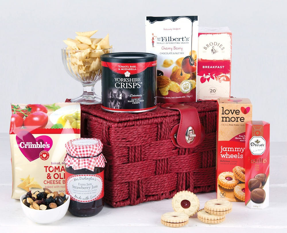 Gluten Free food products including cheese crackers, strawberry jam, jammy wheel biscuits, chocolates, tea, crisps and a cherry berry chocolate and nut mix in a red basket