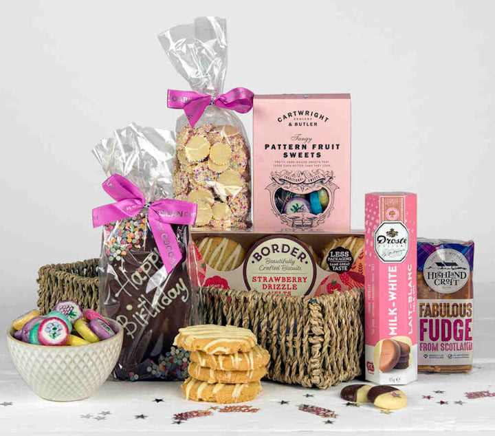 Pink food items including chocolates, fudge, biscuits, sweets and a Happy Birthday Chocolate Bar in a Seagrass Gift Tray