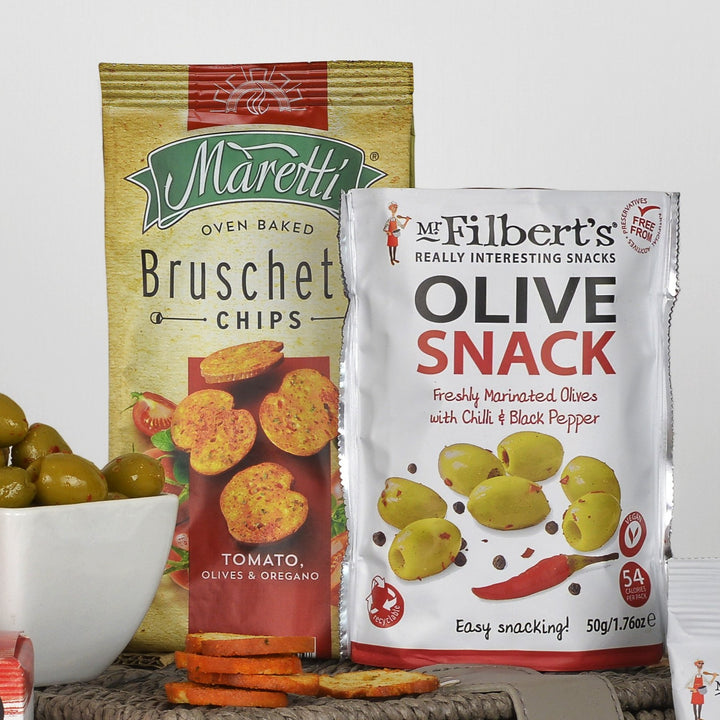 Two snack packages displayed together on a basket: a bag of Maretti Bruschetta Chips and a pouch of Mr. Filbert's Olive Snack.