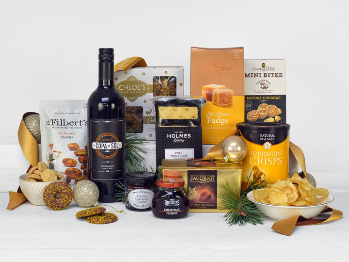 A bottle of red wine with mince pie slices, cheesy bites, crisps, fudge, preserve, chutney, nuts, biscuits and chocolates