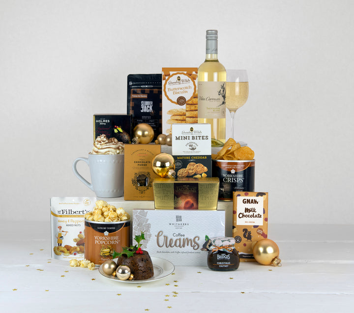 A bottle of white wine and christmas treats such as christmas pudding, christmas chutney, hot chocolate, biscuits, chocolates, popcorn and some savoury treats 