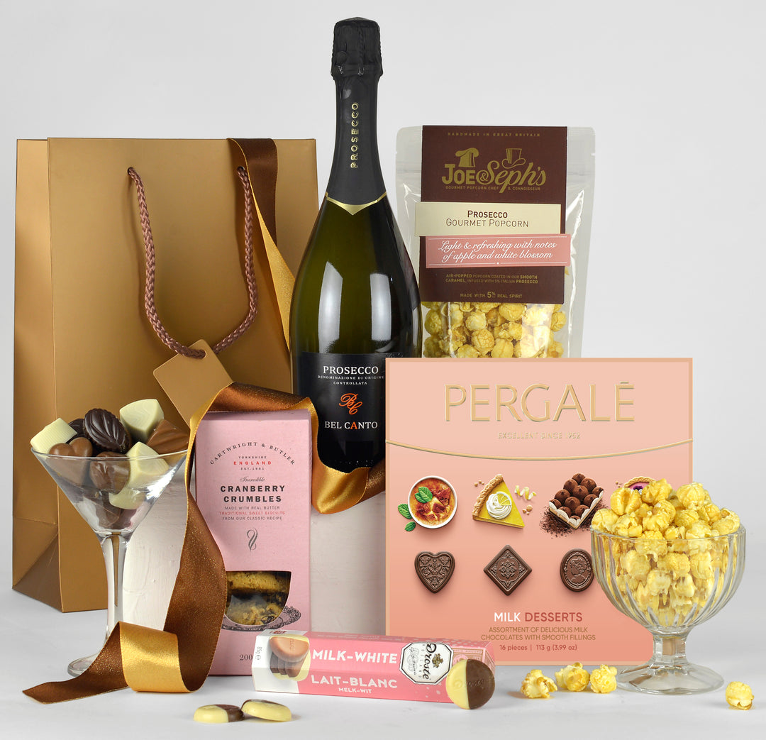 A bottle of prosecco, biscuits, popcorn and chocolates in a gold gift bag