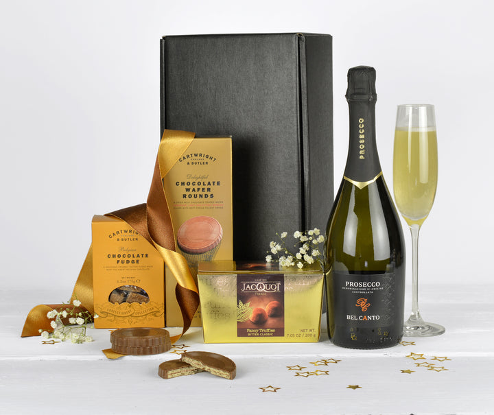 A bottle of prosecco, chocolate biscuits, chocolate fudge and french truffles in a black gift box