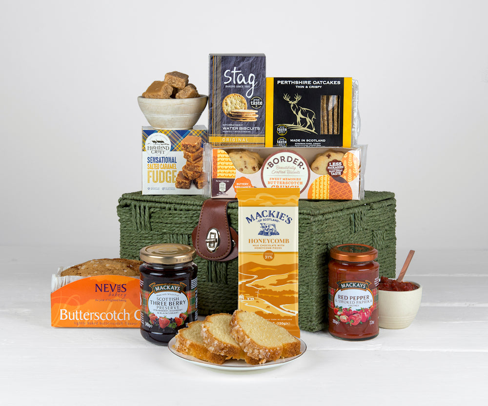 Scottish food including biscuits, chocolate bar, cake, preserve, chutney and other tasty snacks in a green gift basket