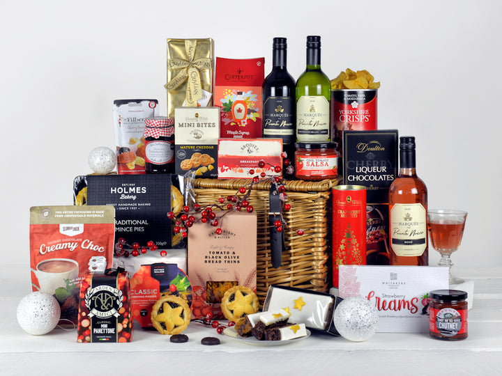 a selection of wines, christmas pudding, mince pies, biscuits, chocolates and other tasty festive food in a wicker basket