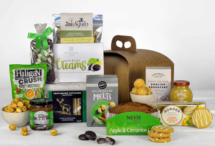 a selection of green and yellow themed treats including cake, popcorn, chocolates, tea and savoury snacks in a gift box